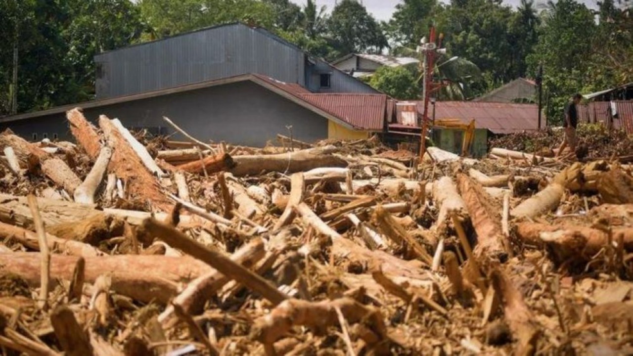 Warga melintas di antara tumpukan gelondongan kayu di permukiman di Tabiang Bandang Gadang, Nanggalo, Padang, Sumatra Barat, Selasa (9/12/2025). (Foto: Antara)